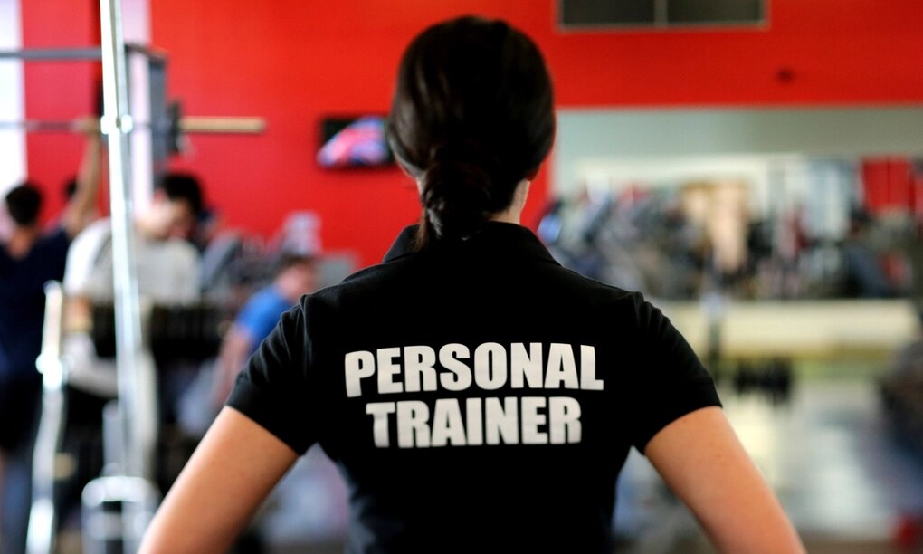Back view of a personal trainer standing in a gym with a red wall