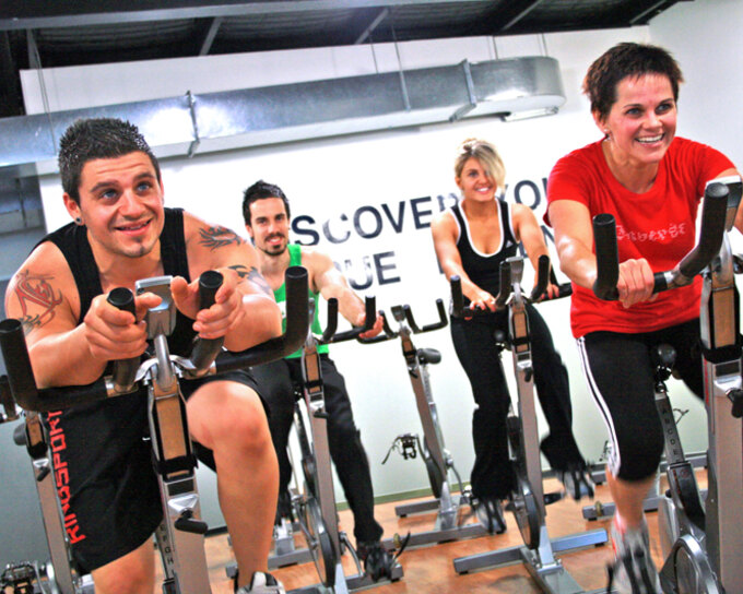 Group indoor cycling class with women riding at the front